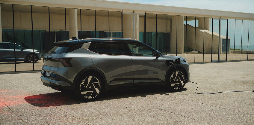 Ein grauer Mitsubishi Eclipse Cross steht mit eingestecktem Ladekabel vor einer Galerie.