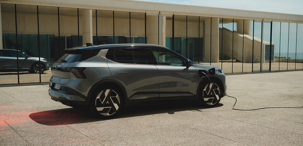 Ein grauer Mitsubishi Eclipse Cross steht mit eingestecktem Ladekabel vor einer Galerie.