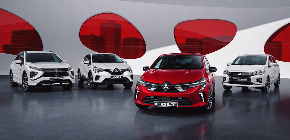 Ein weisser Eclipse Cross, ein weisser ASX, ein roter COLT und ein weisser Space Star stehen aufgereiht vor einer wei&szlig;en Wand mit roten runden Fenstern.