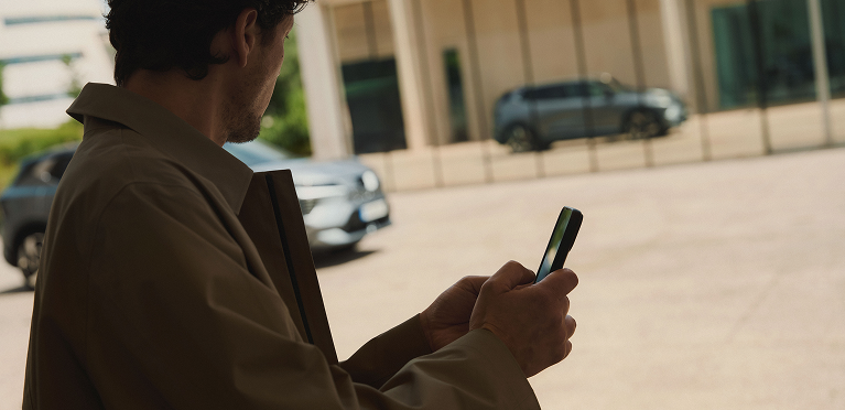 Mann mit Handy in der Hand betrachtet den vorbeifahrenden Eclipse Cross