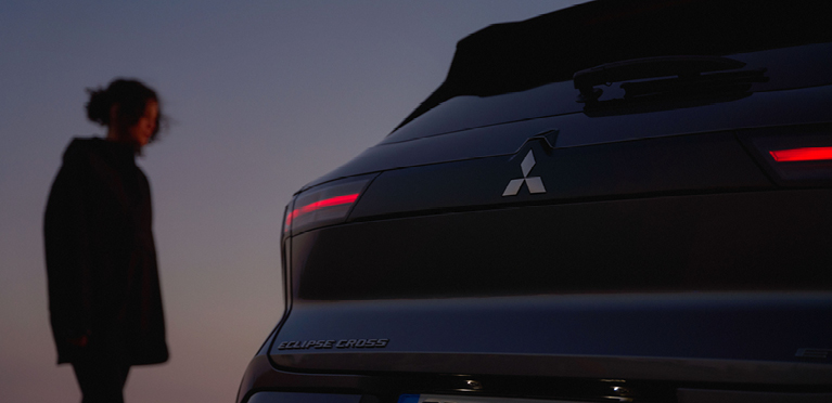 Eine Frau betrachtet das Heck des neuen Mitsubishi Eclipse Cross in der D&auml;mmerung.