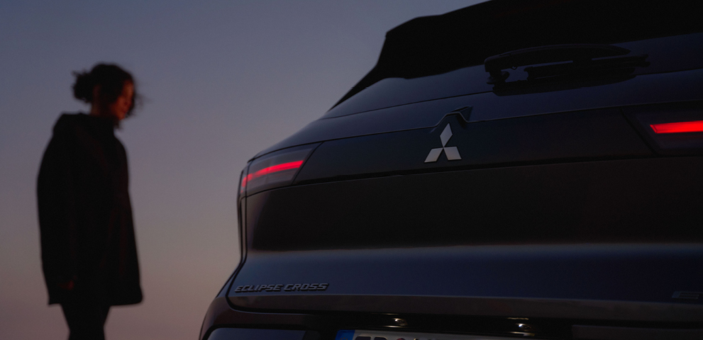 Eine Frau betrachtet das Heck des neuen Mitsubishi Eclipse Cross in der D&auml;mmerung.
