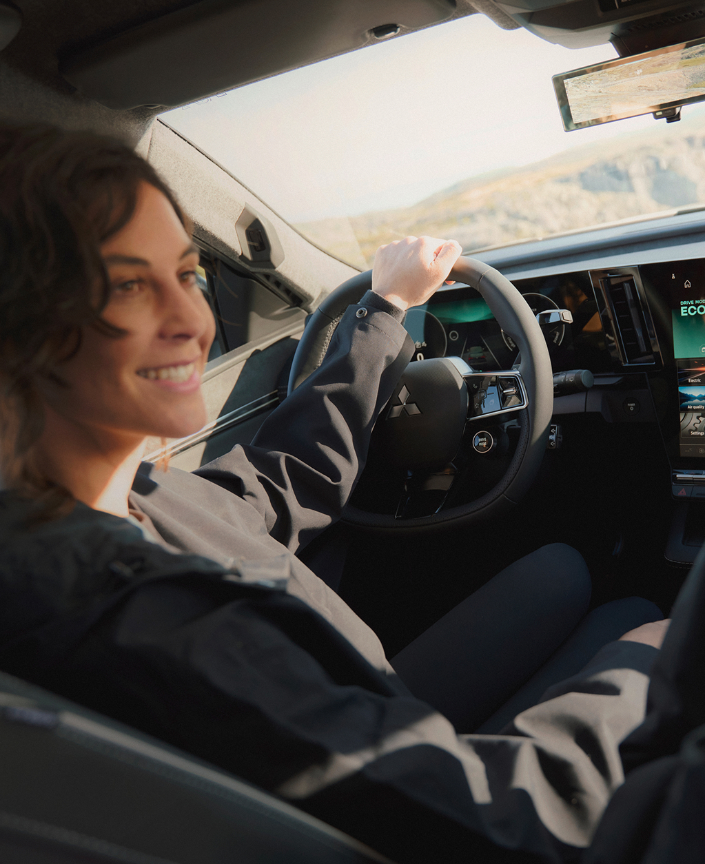 Eine Frau schaut auf dem Fahrersitz sitzend zu ihrem m&auml;nnlichen Beifahrer, auf dem Infotainment erkennt man die Fahreinstellung ECO.