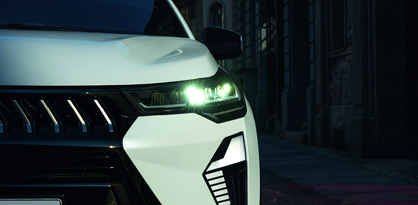 Detailaufnahme der Front eines wei&szlig;en Mitsubishi Grandis SUV in der Stadt, mit eingeschalteten LED-Scheinwerfern und markantem Tagfahrlicht-Design.