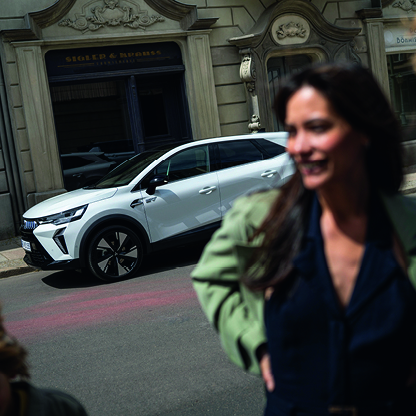 Wei&szlig;er Mitsubishi Grandis SUV vor einem historischen Stadtgeb&auml;ude, im unscharfen Vordergrund eine lachende Frau in Bewegung.