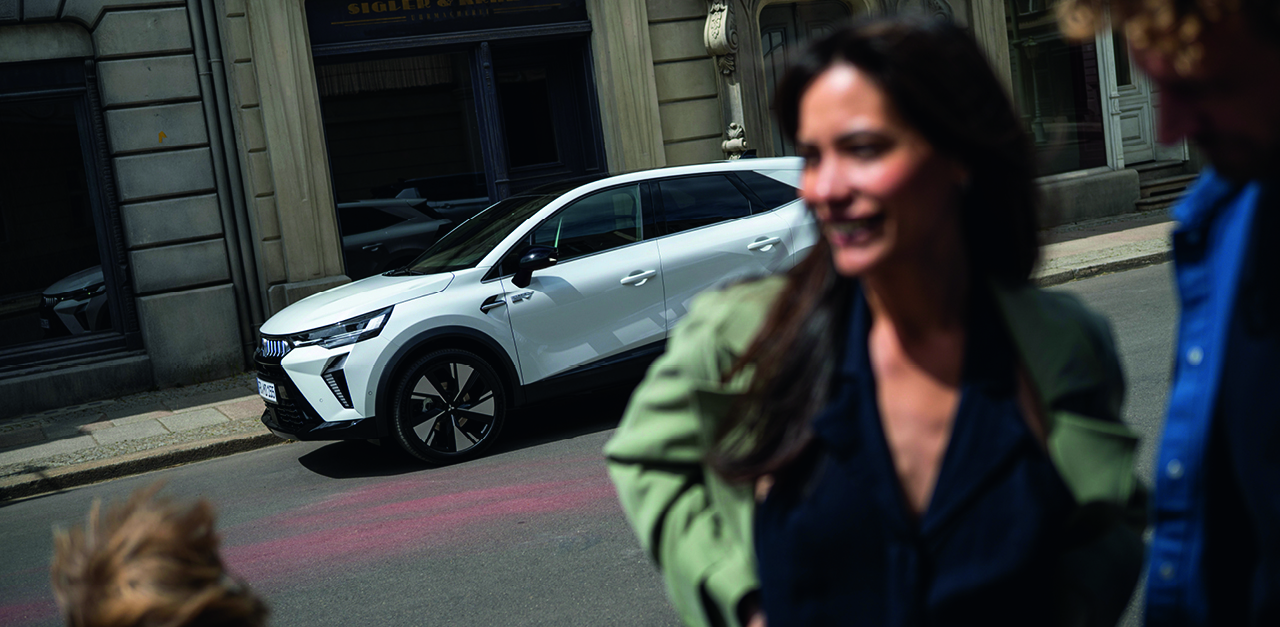 Wei&szlig;er Mitsubishi Grandis SUV vor einem historischen Stadtgeb&auml;ude, im unscharfen Vordergrund eine lachende Frau in Bewegung.