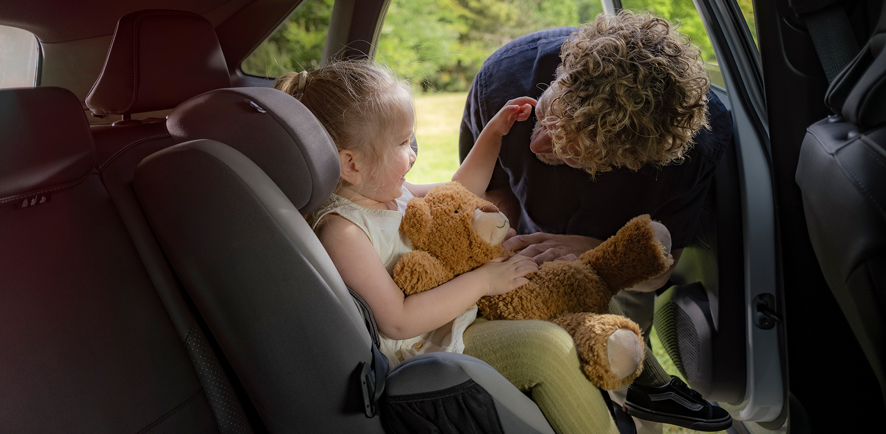 Vater schnallt seine Tochter im Kindersitz auf der R&uuml;ckbank an