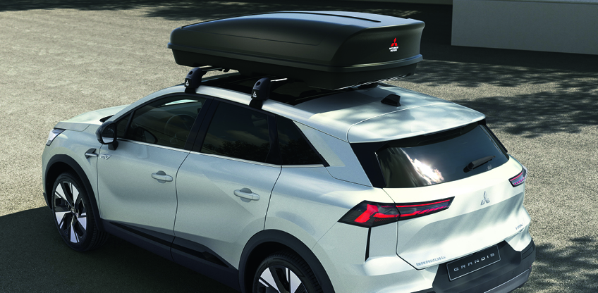 Wei&szlig;er Mitsubishi Grandis mit gro&szlig;er schwarzer Dachbox auf dem Dach, schr&auml;g von hinten oben aufgenommen.
