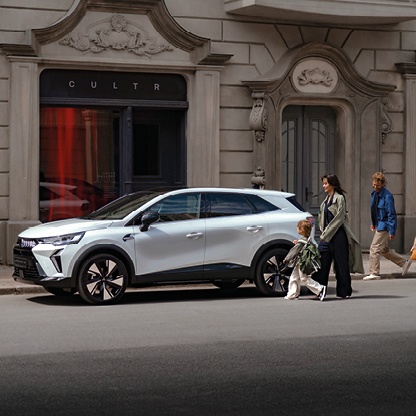 Wei&szlig;er Mitsubishi SUV in der Seitenansicht, geparkt in einer Stadtstra&szlig;e vor einem Geb&auml;ude, mit einer Frau und einem Kind sowie einem weiteren Passanten im Hintergrund