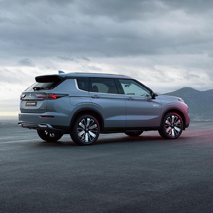 Silberner Mitsubishi Outlander Select in der Heckansicht vor bew&ouml;lktem Himmel und Berglandschaft