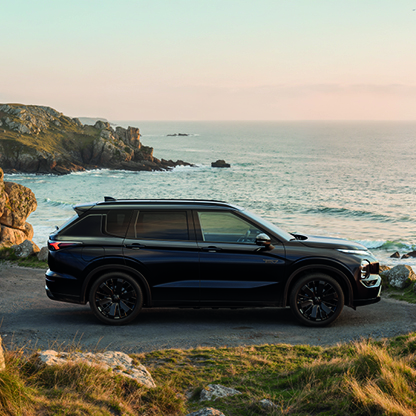 Schwarzer Mitsubishi Outlander Black in der Seitenansicht auf einem felsigen K&uuml;stenweg mit Meerblick im Hintergrund